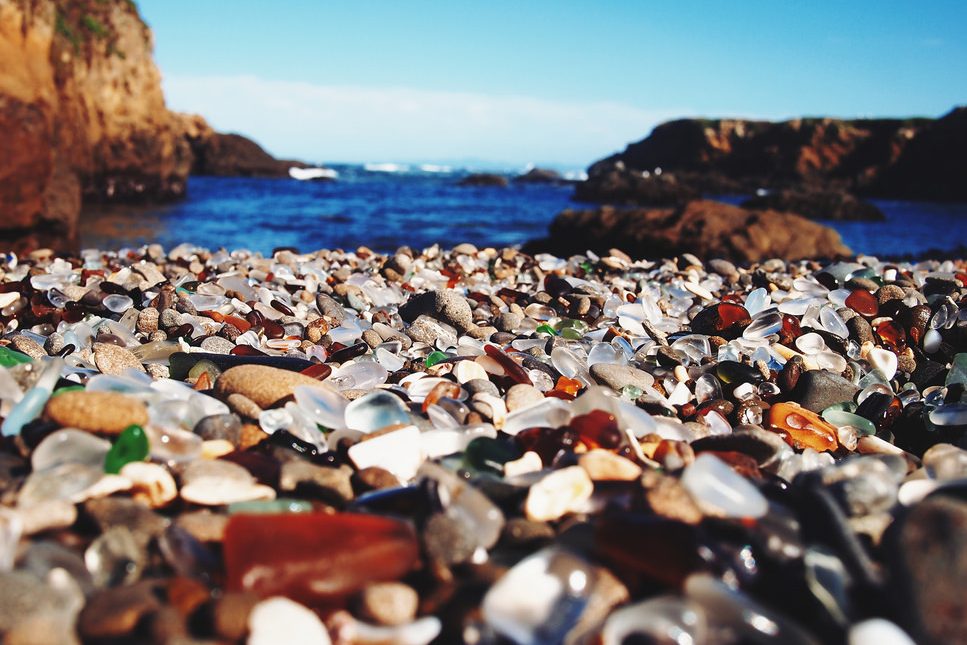 multi-colored seashells and rocks shine in foreground of rocky ocean coast