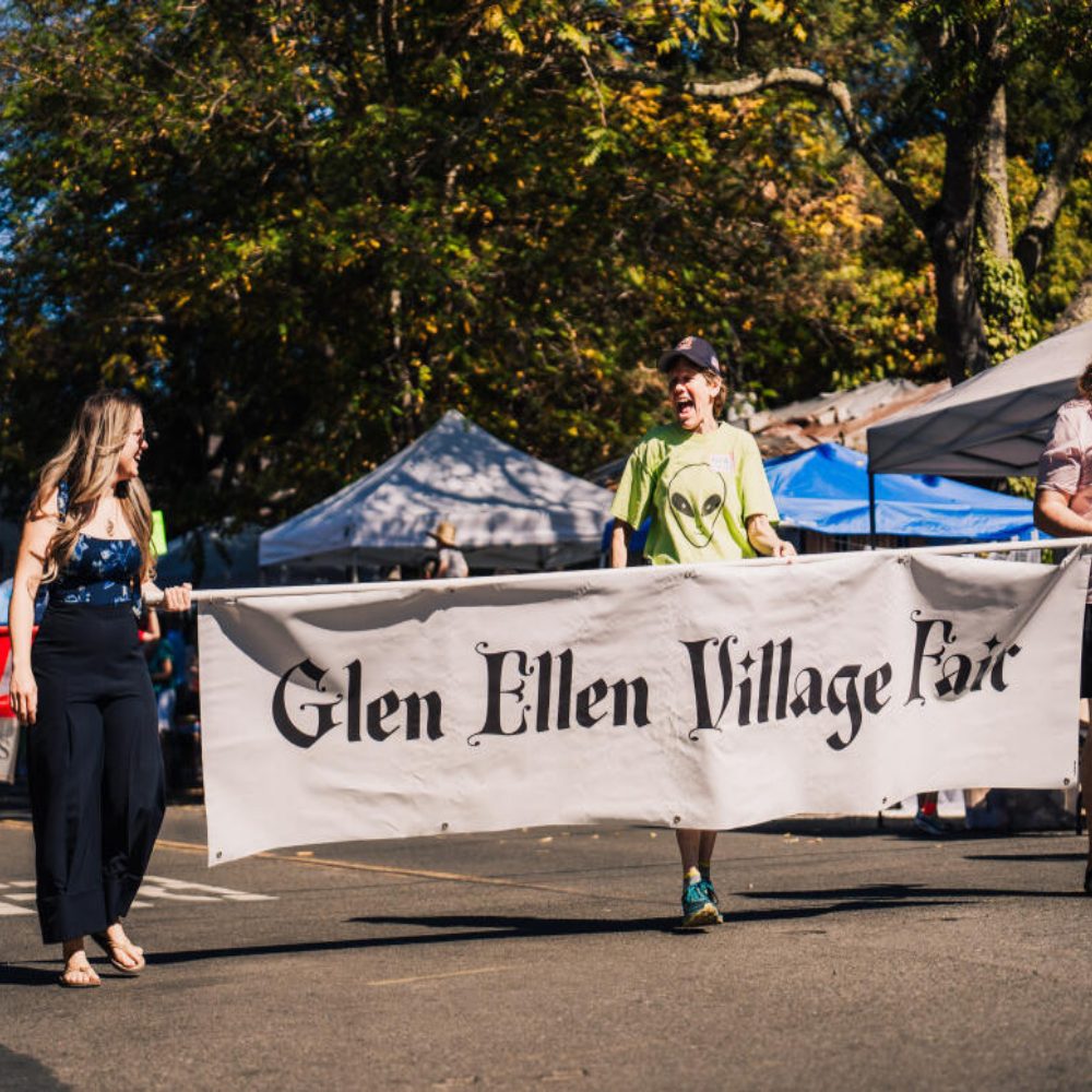 Two people walk with a banner that reads Glen Ellen Village Fair.