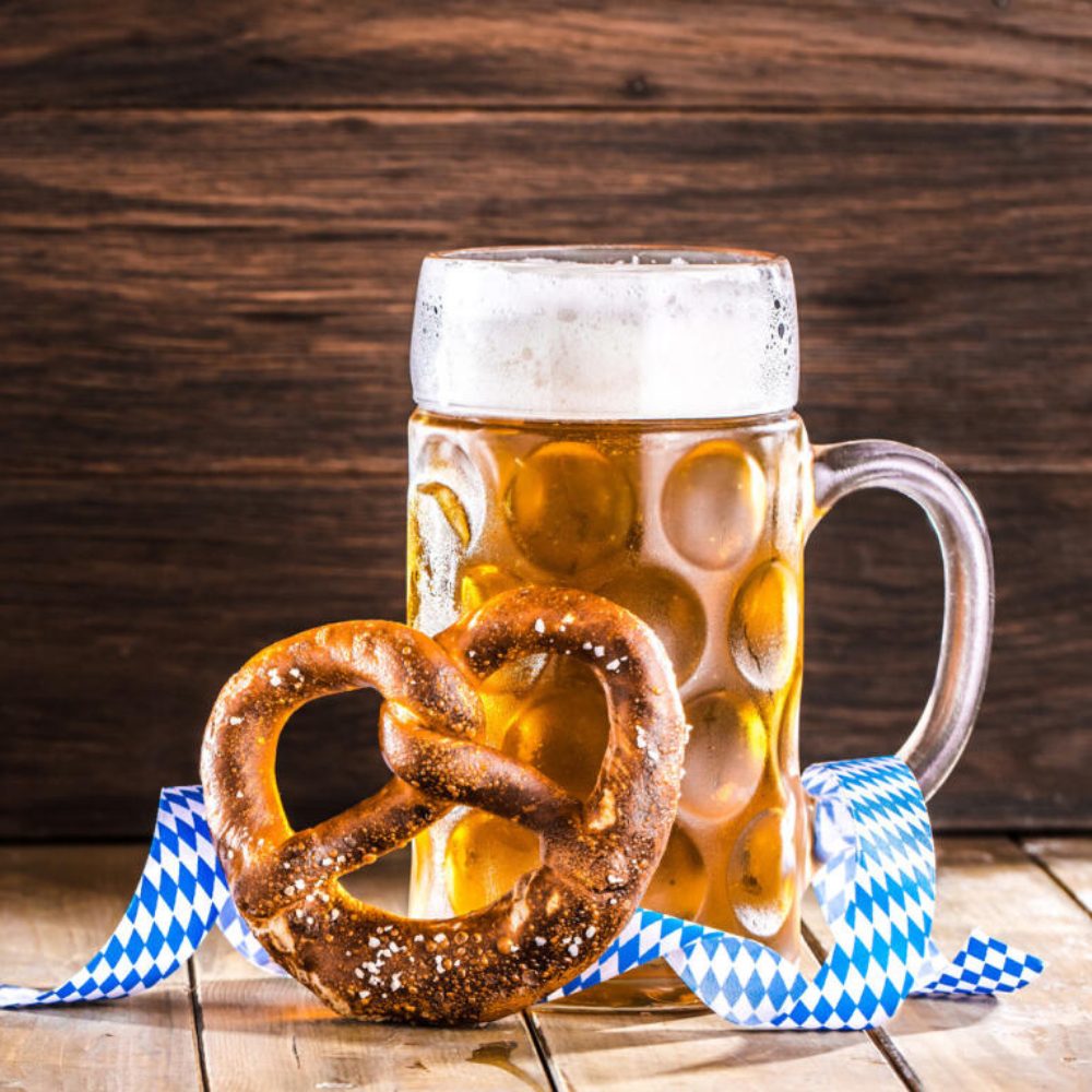 A large glass is full of an amber liquid, a large pretzel leans against it.